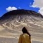 Tourists hiking across Egypt’s Black Desert, surrounded by volcanic black hills and golden sand dunes under the clear Western Desert sky.