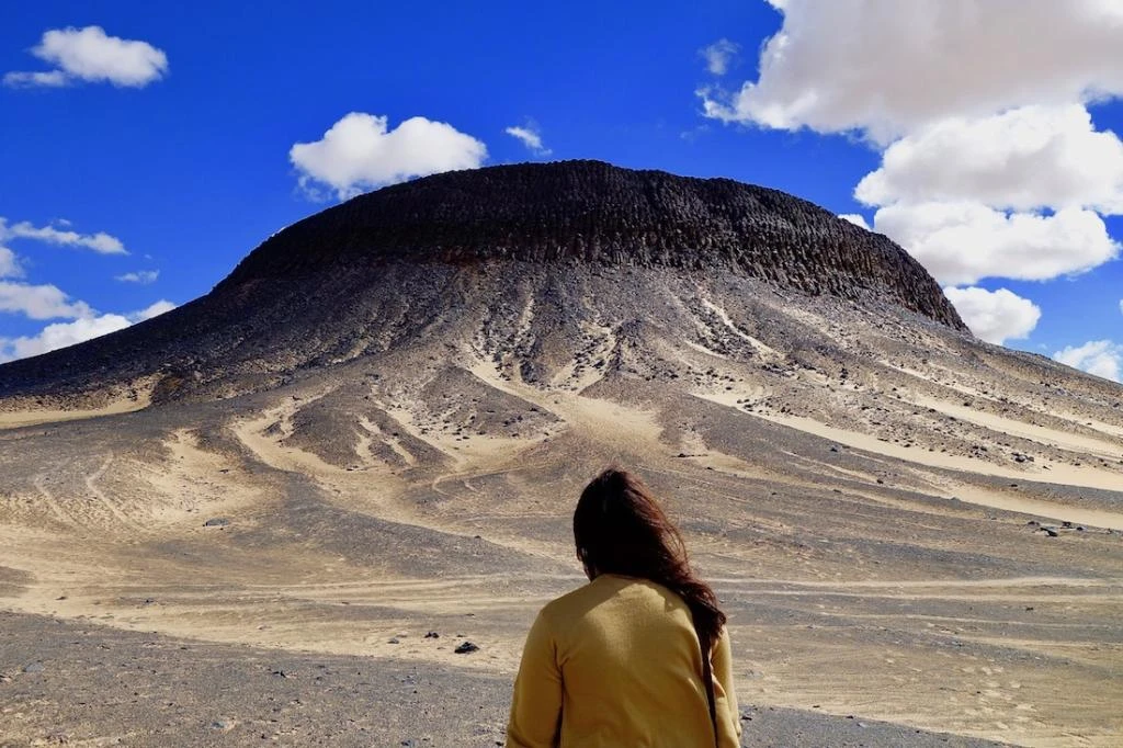 Tourists hiking across Egypt’s Black Desert, surrounded by volcanic black hills and golden sand dunes under the clear Western Desert sky.