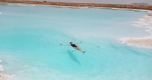 Solo traveller walking near salt lakes in Siwa Oasis, Egypt, surrounded by desert dunes and palm trees.